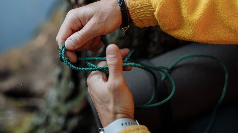 Hands hitching green cord around a tree