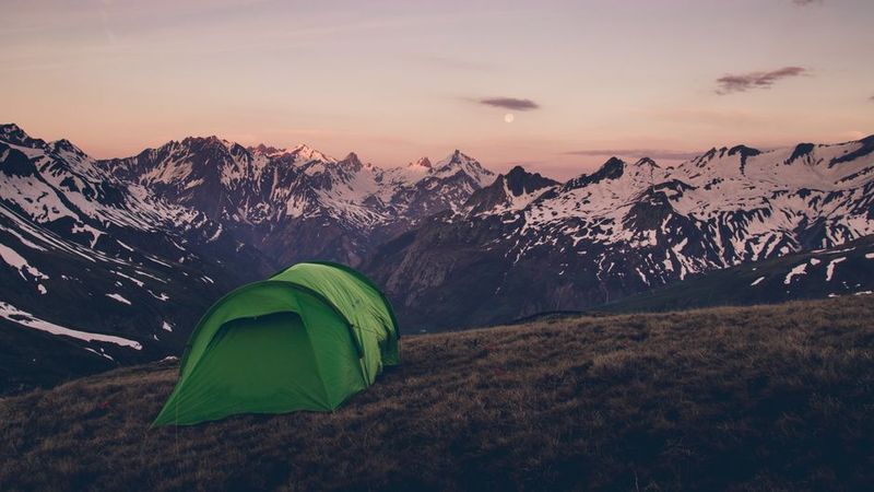 Green tent below alpine peaks at dusk